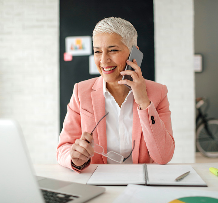 Business woman in blazer smiling while on her smartphone looking at her laptop.