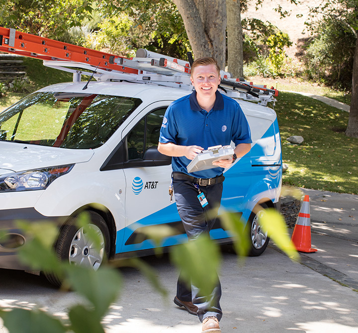 AT&T installation technician walking up the driveway with AT&T van in background. 