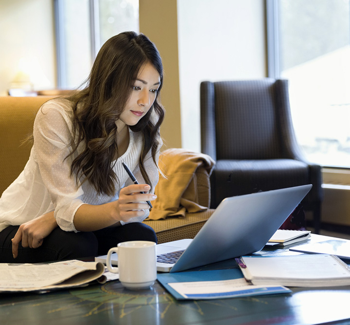 Woman working on a laptop at a coffee table in a lobby. 