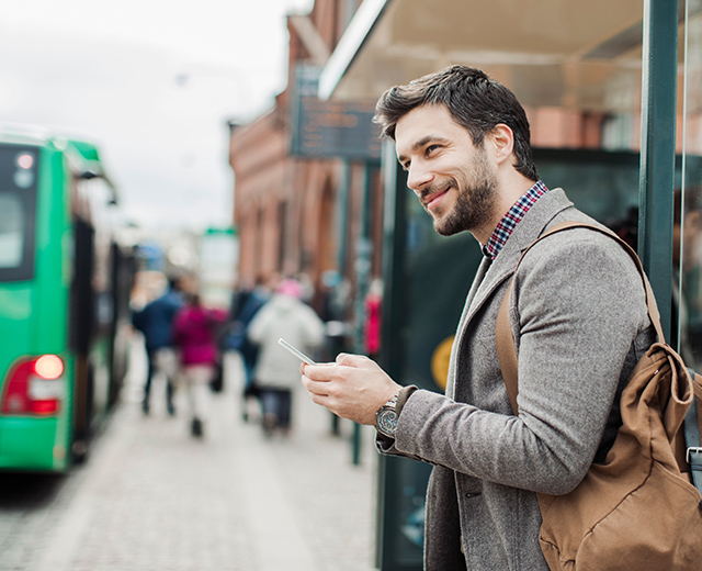 Business man in suite holding the cell phone and standing at the public transport station