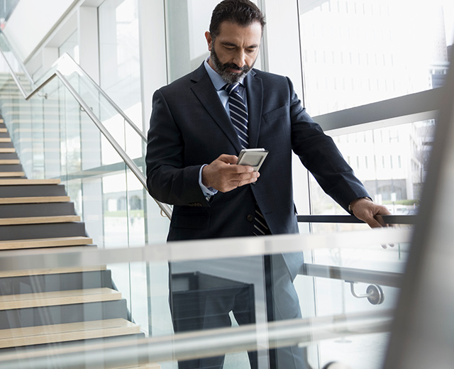 Business man in black-blue suite standing in a hall-way and texting on mobile phone