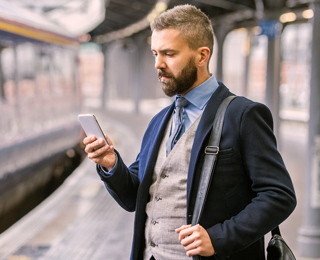 Man in blue suite standing in train station and looking at his mobile phone business messages & apps