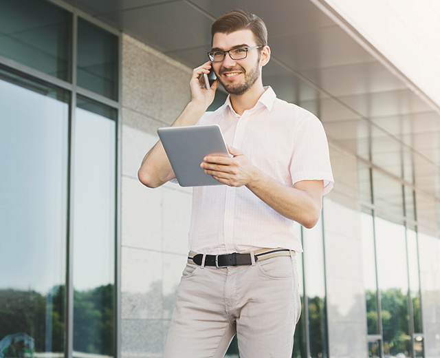 Man walking with iPad in hand and talking on cell phone with a smile represents effective mobile device management