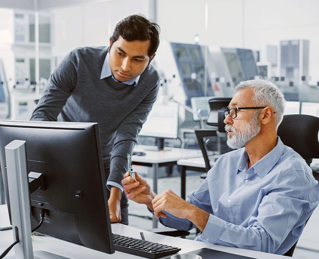 Two men having a discussion in front of a computer monitor.